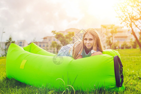 充气风格年轻女人躺在公园的沙发上背景