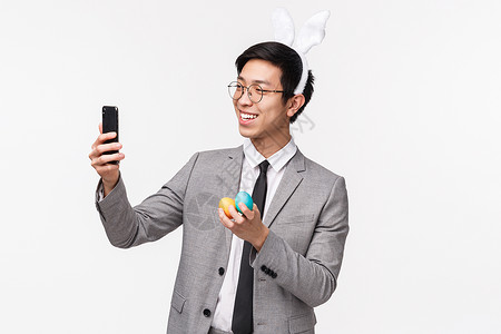 穿西装的兔子假期 人和庆祝活动的概念 穿着西装的年轻快乐愚蠢的亚洲男人的腰上画像 戴着兔耳 用彩蛋自拍庆祝复活节 白色背景背景