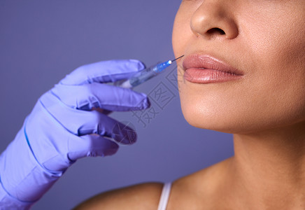 注射美容 美容手术 丰唇和矫正概念 女性面部和手部的特写 手术手套中的注射器靠近嘴唇 准备接受美容治疗背景图片