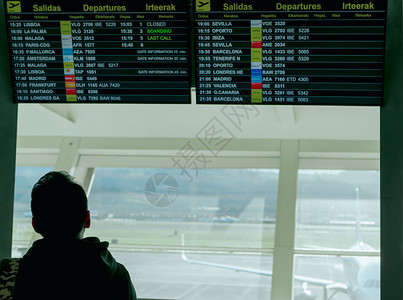 人机场一名男子正在查看信息出发板 并在机场检查他的航班 以便在欧洲旅行 乘客在机场航站楼看时间表数字显示 航班延误的游客背景