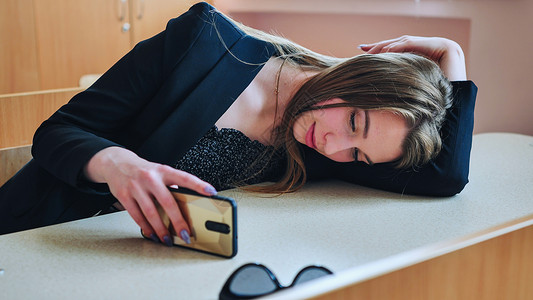 电话对话边框一个躺在她桌上的疲劳学生 看着她的智能手机 然后微笑背景