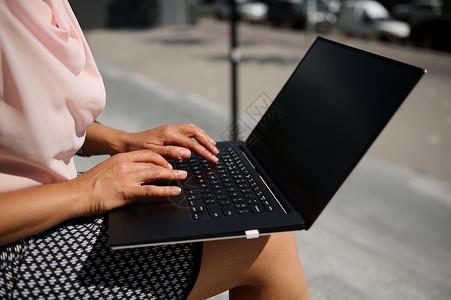 特写女性手在笔记本电脑上打文字的近身 用空白黑监视屏进行输入 同时提供城市背景广告的复制空间背景图片