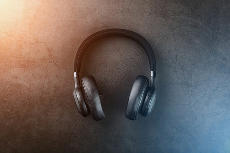 式耳机黑色石材背景上的黑色无线耳机 带有神圣的蓝色和金色光晕 适合 DJ 和音乐家的头顶隔离式专业级耳机体积耳朵阴影技术工作室娱乐音乐背景