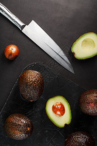 哈斯鳄梨用一把刀切碎了鳄梨 放在黑色纸质黑桌子上 平坦的泥瓦匠蔬菜种子健康食谱饮食木头营养异国香蕉热带背景