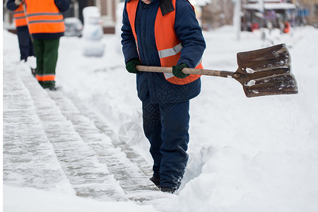 市政部门特殊形式的雇员正在用铲子清除人行道上的雪雪 以特别形式提供市政服务街道男性投掷者工人雪堆橙子降雪职业风暴院子背景图片