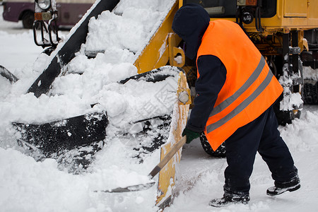 雪犁爪式装载机车辆清除道路上的积雪 市政服务的员工帮助将雪铲入扫雪机背景