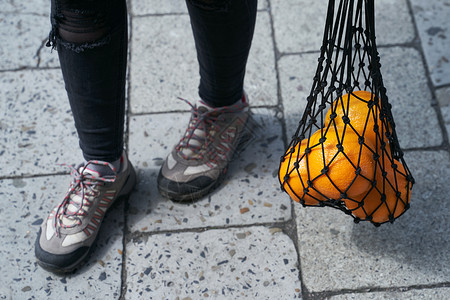 去哪网年轻女子的脚和黑网目袋 满满橘子水果背景