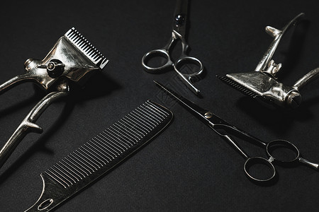 在黑色的表面上是旧的理发工具 两把老式手动理发剪 梳子 美发剪刀 黑色单色 对比阴影 水平的男性马夫奢华修剪理发皮肤剪切安全工作背景图片