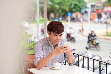年轻微笑的男人在户外咖啡馆看电话或阅读信息教育企业家手机网站细胞工作商务电话人士学生背景图片