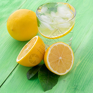 一杯柠檬 半柠檬 绿色桌上新鲜的叶子 用冰 薄荷和小片柠檬来补充冷水 侧视黄色桌子食物树叶水果玻璃饮食热带白色果汁背景图片