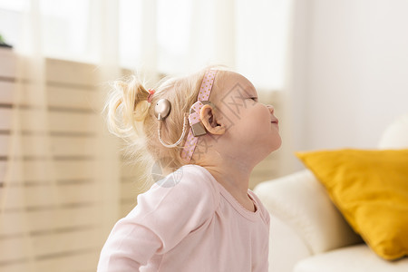 植入人工耳蜗的婴儿在家玩得很开心 耳聋和医疗技术概念教育仿生微笑聋儿药品玩具女性孩子们听力学助听器背景