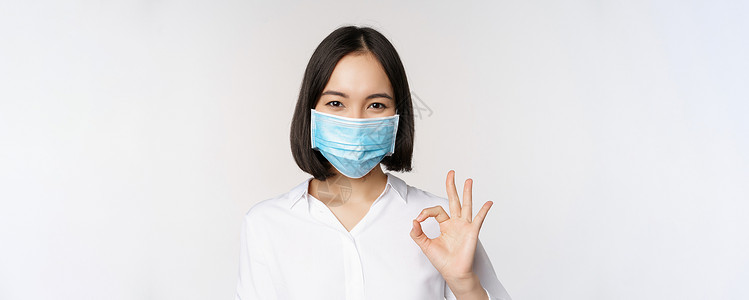 好物推荐Covid 和健康概念 亚洲女性戴着医用面罩 站在白色背景上 表现出好的迹象卫生面具保健冒充员工女士商务成人手臂办公室背景