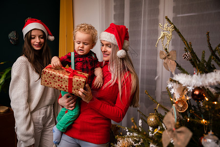 一个妈妈和大姐在圣诞节给一个两岁小孩送礼物幸福孩子圣诞女士儿子气氛传统居家季节彩灯背景