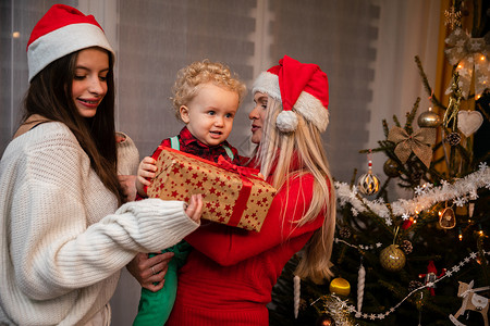 一个妈妈和大姐在圣诞节给一个两岁小孩送礼物儿子金发女郎教导传统气氛假期女士幸福女孩卷发背景