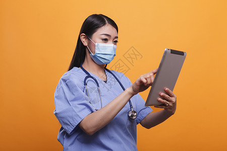 药片和创可贴自信和负责的护士佩戴面部镜和听诊器 使用触摸屏平板背景