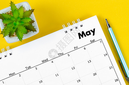 2022年5月的案头日历和笔 还有黄色背景的植物锅背景图片