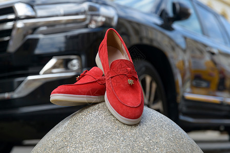 凯乐石女人的红色时装皮鞋 在石头上 车在背景上 一对潮湿的女性面包师鞋子背景