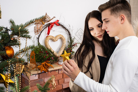 计划一对情侣把金星放在圣诞树顶上 装饰圣诞装饰树的装饰品呢季节庆典氛围恋爱幸福气氛节日男人夫妇拥抱背景图片