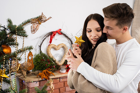 计划一对情侣把金星放在圣诞树顶上 装饰圣诞装饰树的装饰品呢工艺风格幸福云杉恋爱家庭拥抱气氛青年女孩背景图片
