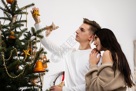 计划一对情侣把金星放在圣诞树顶上 装饰圣诞装饰树的装饰品呢风格喜悦新郎气氛云杉幸福氛围拥抱装潢季节背景图片