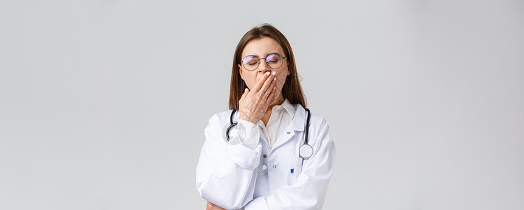 医护人员 医药 保险和 covid19 流行病概念 穿白衣的年轻医生 在冠状病毒期间夜班辛苦的女医生 打哈欠 捂嘴疾病药品装备实背景图片