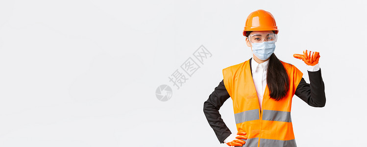 装修宣传折页Covid19 在企业 建设和预防病毒概念方面的安全协议 自信的亚洲女工程师戴着头盔和面罩指着自己 宣传个人协助工作办公室协议商背景