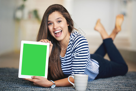 绿屏真实素材这是您想要访问的网站 一个欣喜若狂的年轻女子的肖像躺在家里的地板上 手里拿着一个带有色度键屏幕的数字平板电脑背景