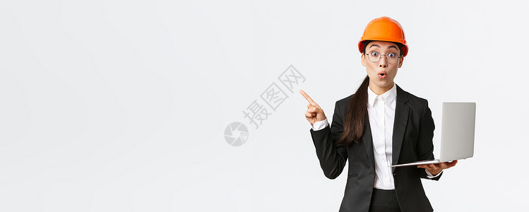 工厂的亚洲女企业家印象深刻 戴着安全帽和西装 手指向左 手持笔记本电脑 在企业展示图表 白色背景房地产经理人士技术商业领导者建筑背景图片