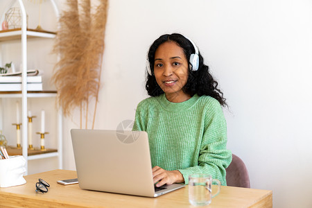 非裔美国人女性在耳机笔记本电脑上工作 在线收听音频播客背景
