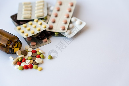 医学和药丸 在白色背景特写镜头的多色药物 棕色玻璃桶和药片在白色背景上 从倒置的罐子中溢出到白色表面的多色药片治疗抗生素疼痛止痛背景