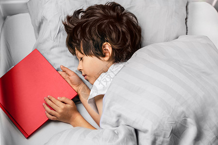 男孩晚上睡在床上 带着一本红书睡眠卧室时间就寝说谎微笑故事孩子孩子们阅读背景图片
