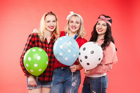 钓友派表情有气球的愉快的女朋友 三个开朗美丽和时尚的女孩拥抱并且对着镜头微笑的库存照片 他们拿着五颜六色的点状气球 在红色背景上隔离黑发友背景