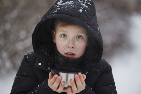 很热小男孩一个戴兜帽的小男孩在冬天拿着一个杯子背景