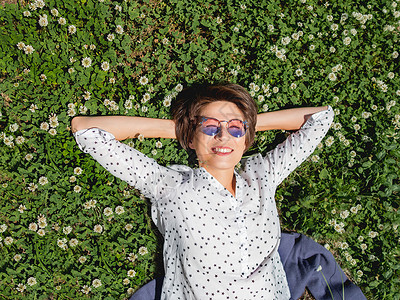 榆柳荫后檐城市公园草坪上青柳花中躺着的女人的顶级视野 镇上的自然 下班后户外放松 夏季气氛背景