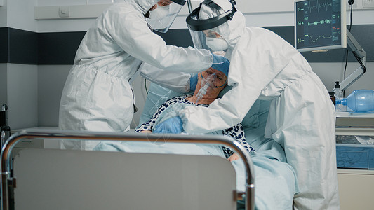 使用氧气管 配有防护制服的医疗队男人病人监护病房封锁管子传染性退休重症护理人员背景