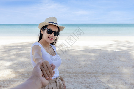POV 观点跟着我戴墨镜的女人手牵着男朋友去海边 看着相机 走在海滩的愉快的女孩后面看法 夫妇在海滩上度假旅行 暑假日落女士微笑背景图片