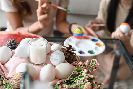 彩蛋中的女孩在客厅的桌上放满鸡蛋和鲜花的Wicker篮子 母亲和女儿在背景中绘画复活节彩蛋背景