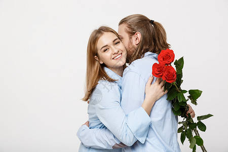 一位有魅力的年轻人向女友隐瞒鲜花 然后在白种孤立的背景下给她一个惊喜 她被描绘成一幅吸引人的肖像周年黑发玫瑰纪念日男朋友微笑情人背景图片