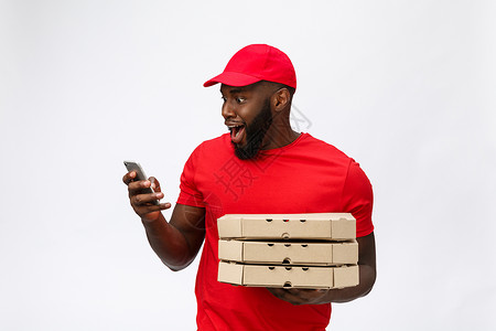 交付概念 英俊的非洲比萨饼送货员用令人震惊的面部表情与移动交谈 孤立于灰色背景震惊工人工作送货说话手机盒子职业技术服务背景图片