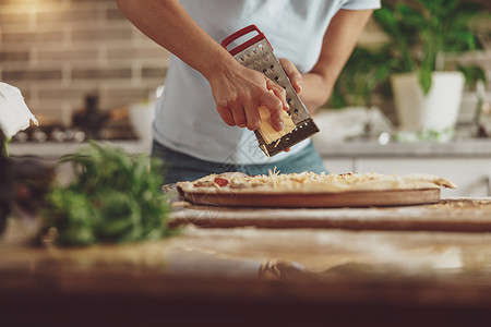 家庭主妇的手用磨刀 同时用奶酪做意大利披萨高清图片