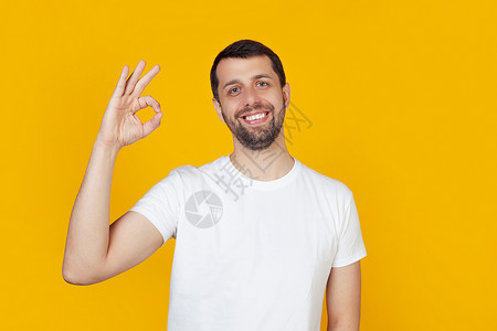 留着胡须的年轻男子穿着白色 T 恤 笑得很开心 微笑着 用手和手指做出好的手势 没关系 幸运的表情 站在孤立的黄色背景上背景