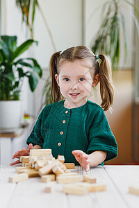 身着绿色衣服和破碎的木制Jennga塔台在桌子上微笑的 又可爱又傻又可爱的孩子背景图片