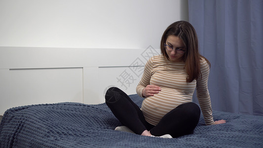 怀着眼镜的年轻孕妇在肚子上摸索 卧室里的那个女孩躺在床上背景图片