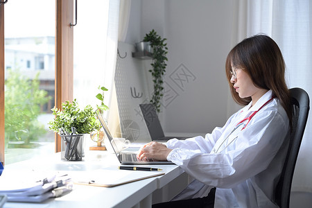 在医疗办公室使用膝上型计算机看穿白制服的女侧边医生图片