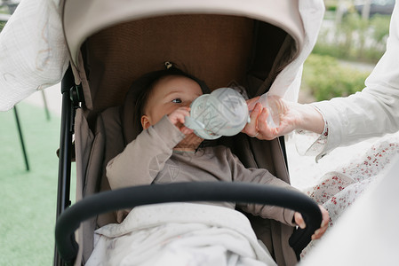 婴儿车里的婴儿正喝着瓶子里的水背景图片