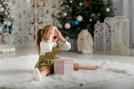 漂亮的粉色圣诞树充满激情的 令人惊讶的情感可爱的女孩 带着新年礼物 坐在圣诞节内地闭着眼睛坐着背景