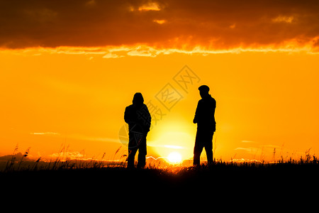 时光请慢些两个男人在日落或日出时与戏剧性的天空和云交谈的剪影 对话和在地平线和天际线上遇见两个人 阳光下的人的轮廓 与朋友的黄金时光背景