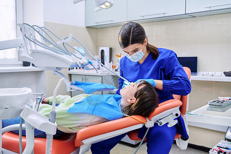 医生牙医治疗一名年轻少女女病人的牙牙牙牙齿青少年款待面具检查卫生搪瓷椅子职业工具背景图片