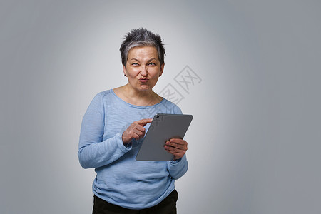 拥有数字平板电脑工作或检查社交媒体的白发成年妇女 50多岁穿蓝衬衫的美貌女性在白色背景上与白人隔绝了50多岁背景图片