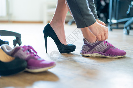 足部疼痛的办公室女员工腿部特写 一位女士将黑色绒面革高跟鞋换成了更舒适的鞋子 女孩脱下鞋子 换上紫色的跑鞋公司运动鞋扶手椅鞋类地背景